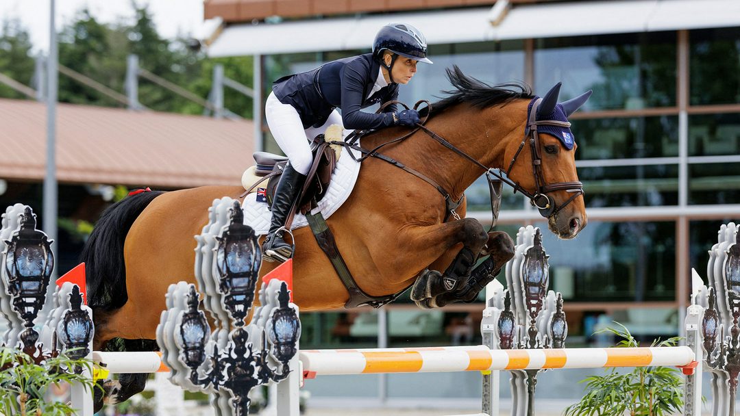 Australian rider Edwina Tops-Alexander clears a large oxer of white and yellow poles riding Fellow Castlefield